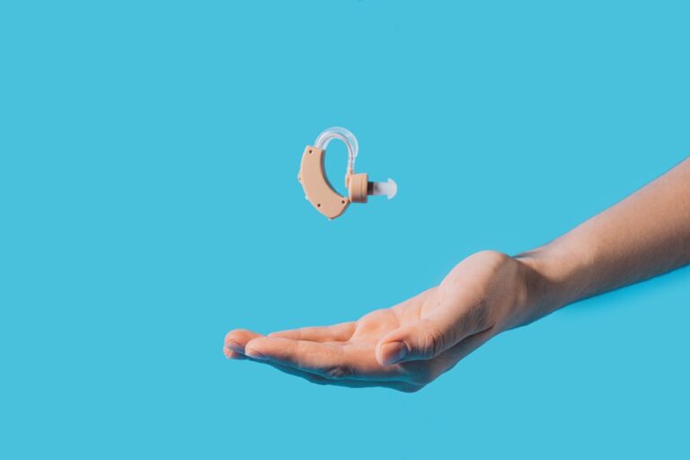 Hearing aid hovering above the hand against a blue background