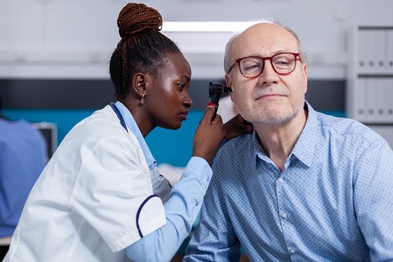 Black doctor with metal tool for ear checkup and stethoscope checking on senior man