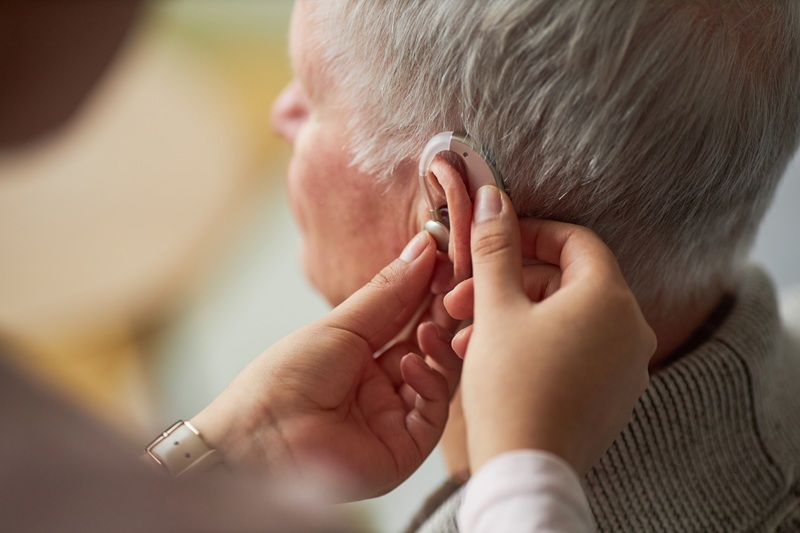 Close-up of social worker caring about senior man with deafness, she wearing hearing device on his ear