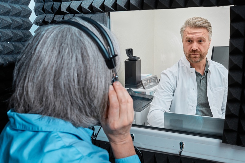 Audiological exam. Audiologist doing hearing check-up to gray-haired woman in soundproof audiometric booth with audiometer