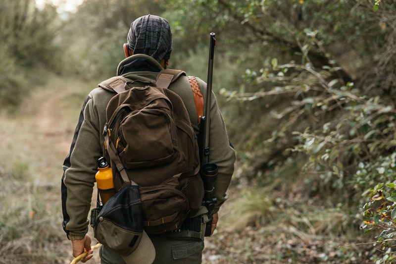 Hunter is making his way through a dense forest path, equipped with a rifle and a backpack