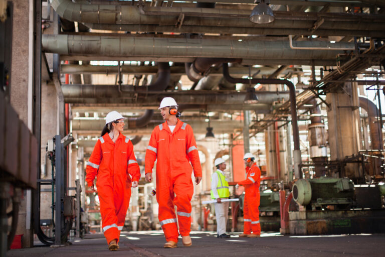 Factory workers wearing ear protection and hard hats walking through a noisy industrial plant, representing occupational noise exposure linked to industrial deafness claims