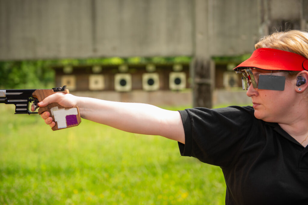 Competitive shooter wearing custom-fit shooting ear protection while aiming a pistol at an outdoor range