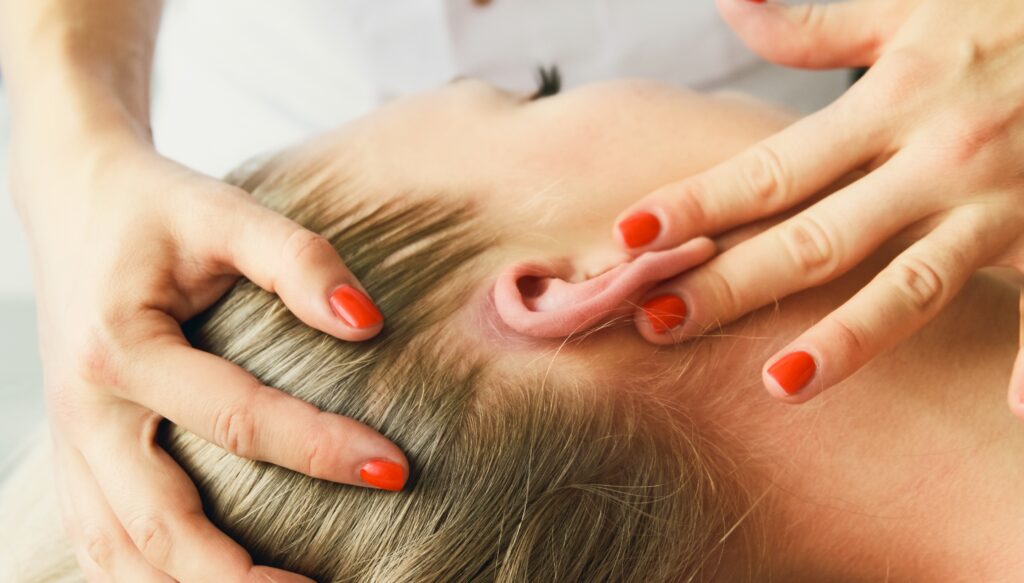 Practitioner with red nails gently massaging a young child’s ear and scalp during a relaxing ear care session